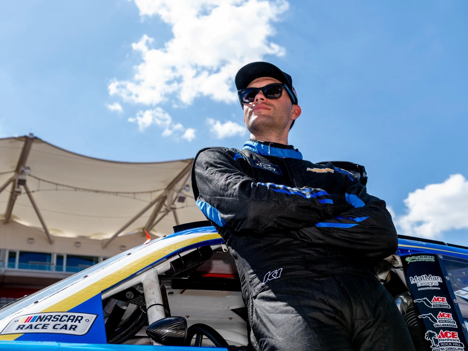 Baltazar Leguizamón con traje negro y azul en el paddock de NASCAR
